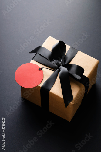 Gift box with black bow and red price tag on black background.