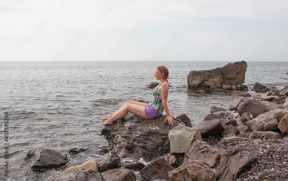 young girl sitting on coastal stones by the sea