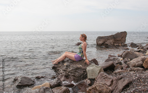young girl sitting on coastal stones by the sea © Наталья Жукова