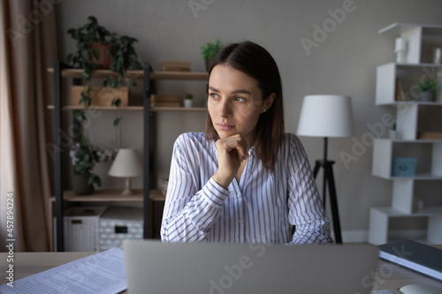 Tableau sur toile Pensive woman looking in distance, sitting at work desk with laptop, thoughtful