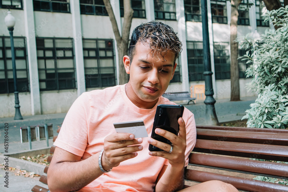 Young latin man purchasing with credit card on internet. E-commerce payment on cellphone. Young latin man purchasing with credit card on internet. E-commerce payment on cellphone.