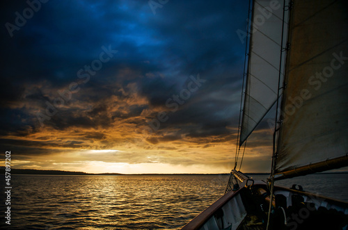 A boat sails towards the sunset under dark clouds