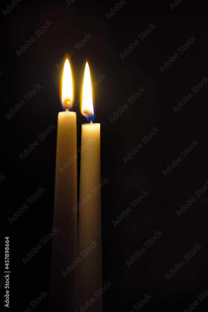 two burning candles on a black background two burning candles on a black background