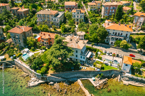 Beautiful villas near the coast of rocky beach in a small town Lovran, Croatia. Arial view of Lungomare sea walkway with transparent water.