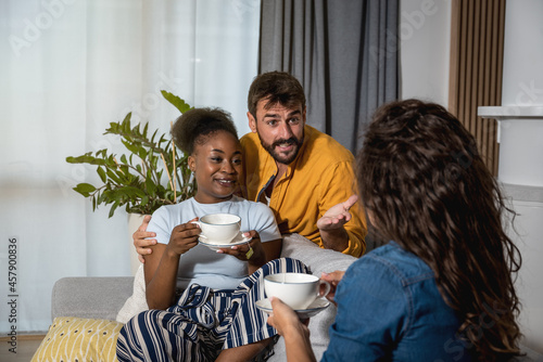 Young mixed-race family hosted their friend as a guest in their apartment over a cup of tea and having fun through conversation they explain to her about their plans for the future