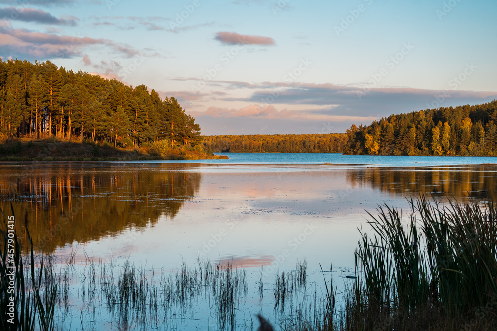 The landscape of the autumn coniferous forest and the sky in the colors of the sunset with a reflection in the water of the lake.
