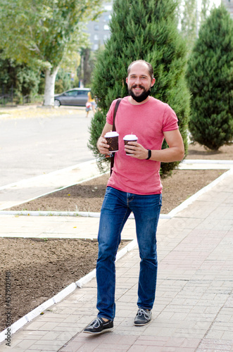 Young man with a beard carries two glasses of coffee in his hands