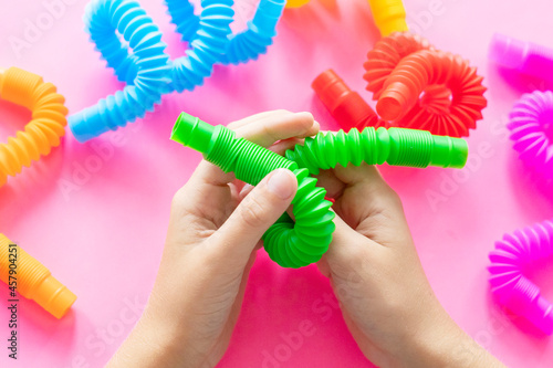 colorful antistress sensory toy fidget push pop tube in kid's hands on pink background photo