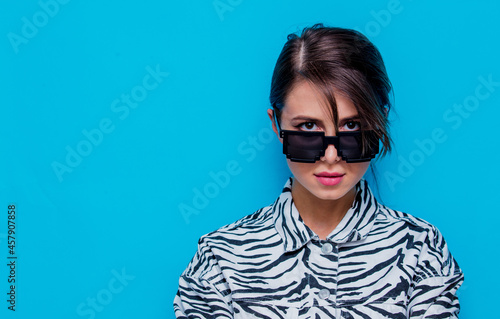 Young woman in zebra clothes and sunglasses on blue background