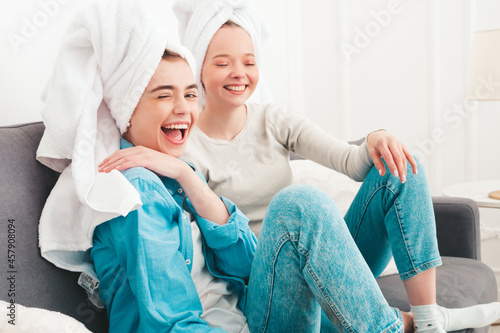 Two young beautiful smiling women sitting at the sofa. Sexy carefree models posing indoors in posh apartment or hotel room. They doing beauty treatments at home in towels on heads