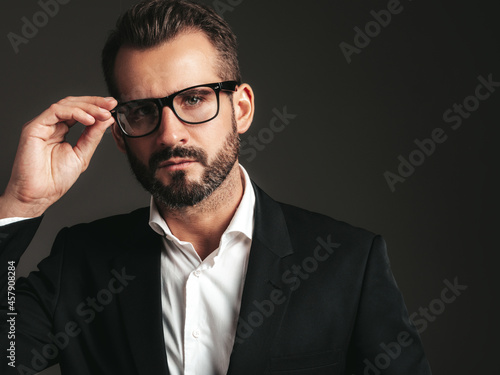 Closeup portrait of handsome confident stylish hipster lambersexual model. Sexy modern man dressed in elegant black suit. Fashion male posing in studio on dark background. In spectacles
