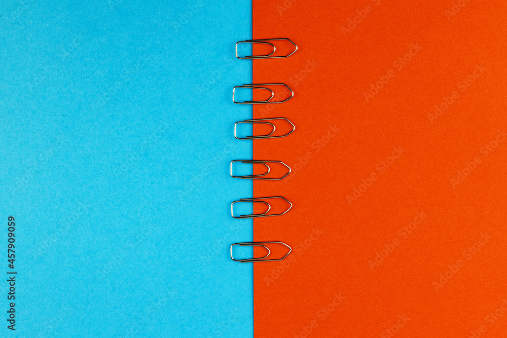 Office paper clip on an orange-blue background. Top view.