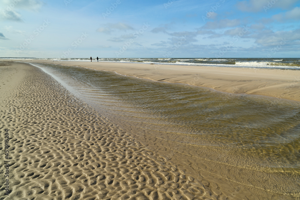 Fototapeta premium Jesienny, zimowy spacer nas morzem. W oddali spacerujące dziewczyny. Ujęcie obiektywem szerokokątnym. Pomarszczona powierzchnia plaży. Po sztormie.