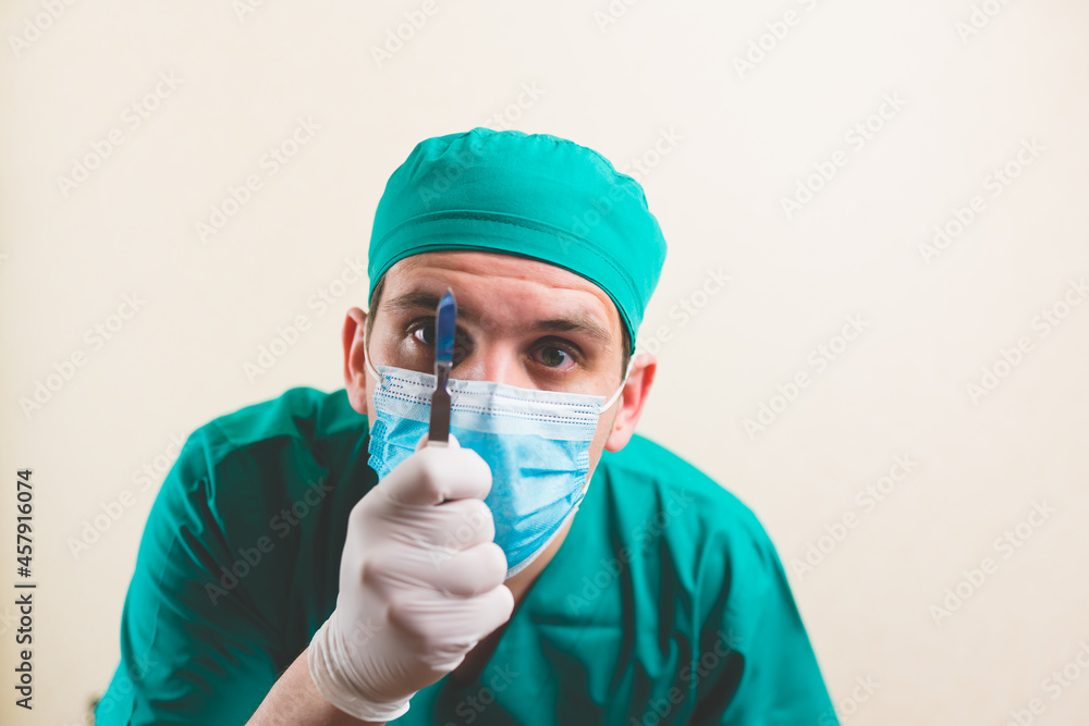 Young doctor in green surgeon suit and protective breathing mask with lancet in hand isolated on the yellow background Young doctor in green surgeon suit and protective breathing mask with lancet in hand isolated on the yellow background