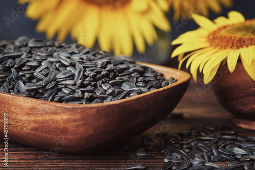 Wooden bowl of sunflower seeds and beautiful yellow sunflowers on background. photo