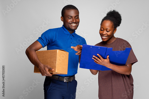 фотографія african lady filling details in a manifest to receive a package from a delivery