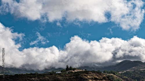 Hyper lapse smooth zooming in twirling clouds on blue sky falling on the top of mountains at a late summer afternoon.