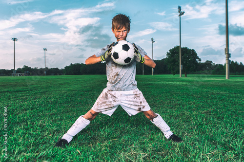 Muddy little soccer player in funny pose trying to crush soccer ball © 3Days2Go Media