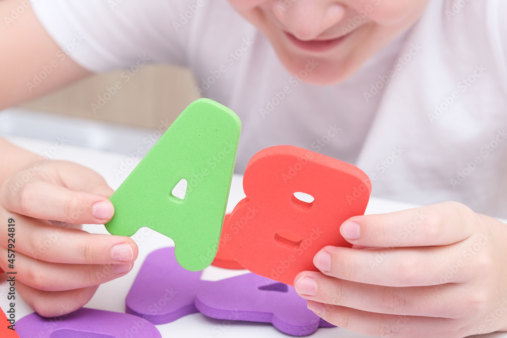 A kid learning letters and alphabet, he is sitting at a table and holding colorful foam letters in hands A kid learning letters and alphabet, he is sitting at a table and holding colorful foam letters in hands