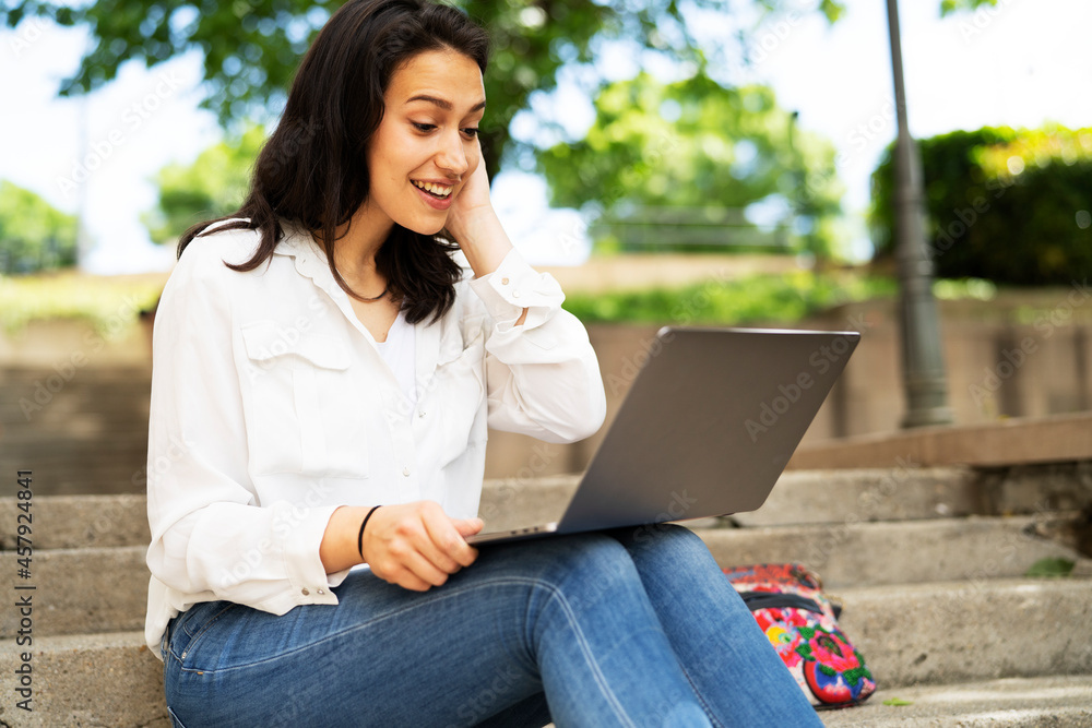 Young businesswoman sitting on steps outdoors and working on laptop. Beautiful girl learning in the park. Young businesswoman sitting on steps outdoors and working on laptop. Beautiful girl learning in the park.