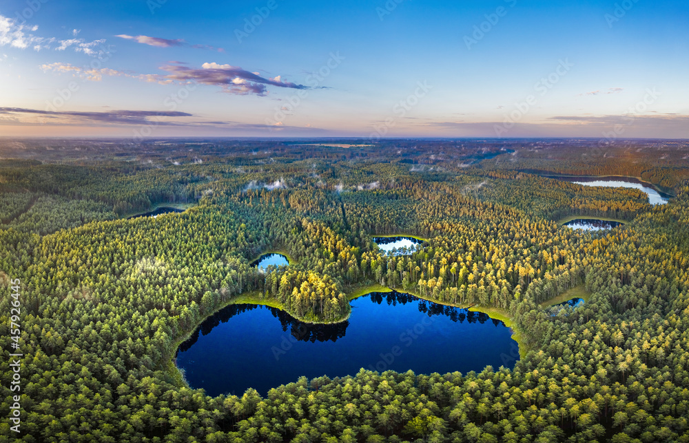 Aerial view of sunrise over a pine forest with lake. Foggy and colorful morning in countryside.