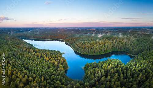 Aerial view of sunrise over a pine forest with lake. Foggy and colorful morning in countryside.