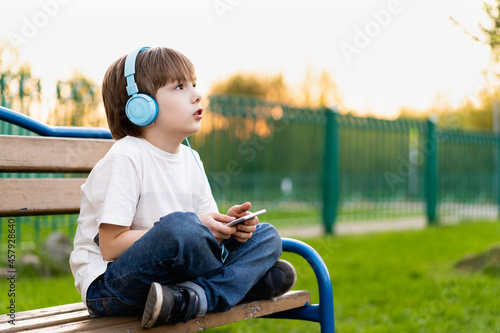 boy on the street sits on a bench with headphones and with a phone © Надежда Урюпина