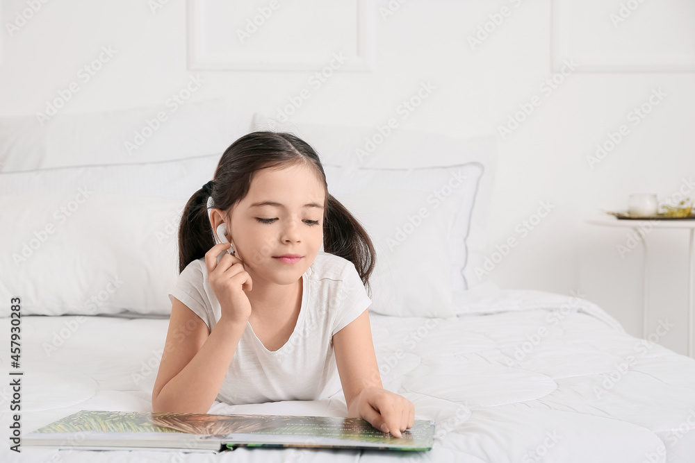 Little girl with earphones reading book in bedroom Little girl with earphones reading book in bedroom