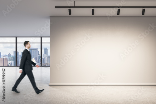 Businessman walking in modern office interior with blank wall, mock up place and window with city view.