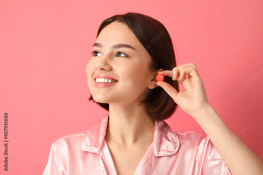 Young woman putting ear plug on pink background Young woman putting ear plug on pink background