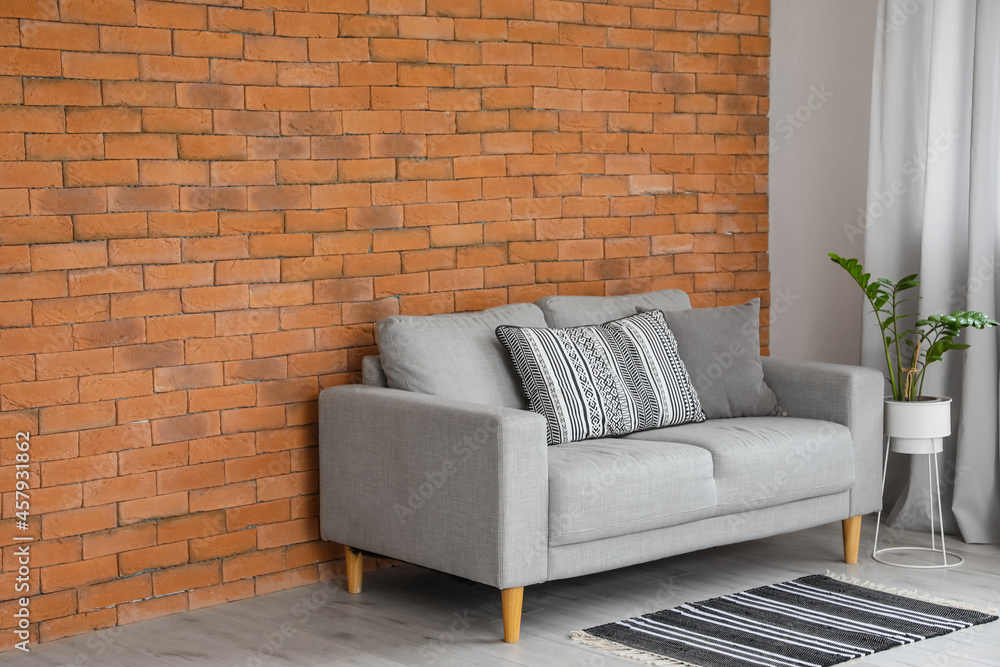 Naklejka premium Modern sofa and houseplant near brick wall