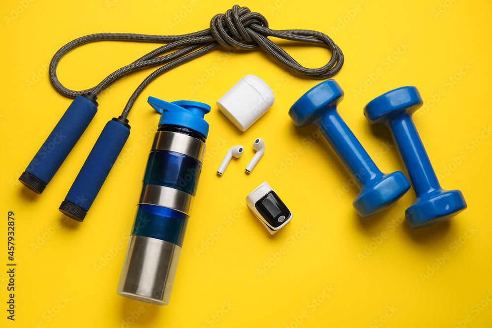 Pulse oximeter, dumbbells, skipping rope, bottle of water and earphones on color background Pulse oximeter, dumbbells, skipping rope, bottle of water and earphones on color background