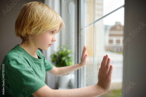Sad little boy is sitting near window and watching street. Lonely at home. No friends, no siblings. One baby in family. Child cannot build relationships with his peers. Upset offended kid. © Maria Sbytova