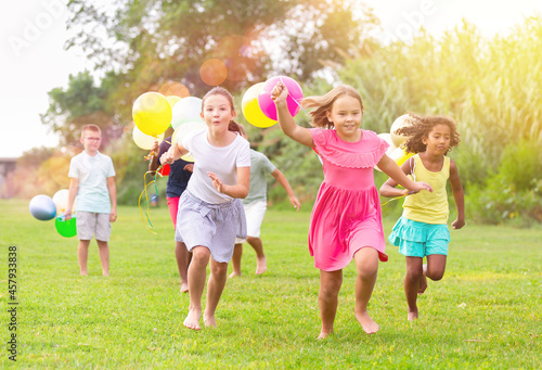Group of happy kids running through grass with balloons in hands.