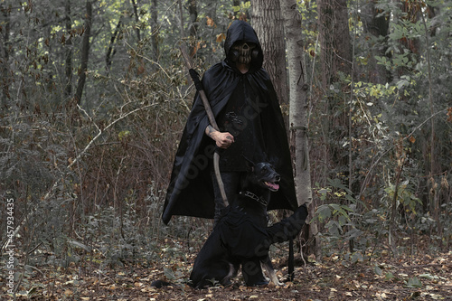 a man in a scary mask and black clothes with a black dog in a gloomy forest.an image for Halloween and the day of the dead