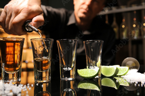 Sticker Bartender pouring tasty tequila into glasses at table in bar, closeup