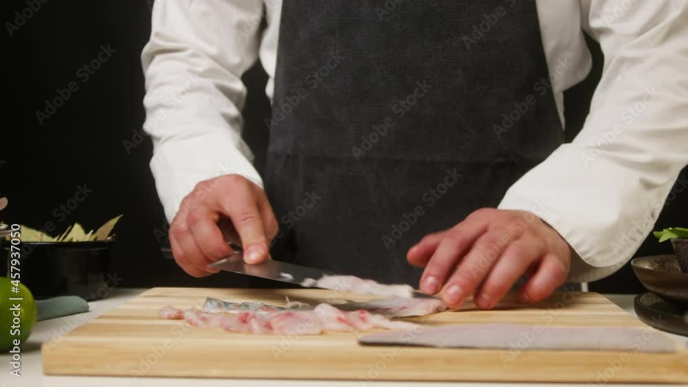 Professional Chef cutting raw white fish close-up, thin slices. Man cooking seafood dishes using sharp knife, wearing apron. Process of preparing ingredients for Peruvian ceviche. Professional Chef cutting raw white fish close-up, thin slices. Man cooking seafood dishes using sharp knife, wearing apron. Process of preparing ingredients for Peruvian ceviche.