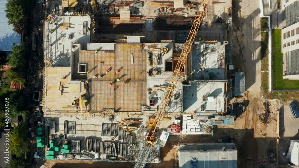 Top view of the construction of the property with tall tower cranes and workers in helmets, heavy equipment is involved at the construction site. Top view of the construction of the property with tall tower cranes and workers in helmets, heavy equipment is involved at the construction site.