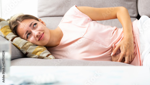 Portrait of depressed girl lying on sofa with stomach problems