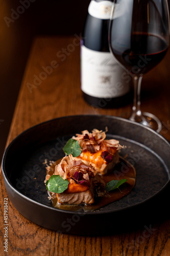 Gourmet salmon steaks with sour-sweet sauce and a bottle of red wine, side view, dark atmospheric restaurant