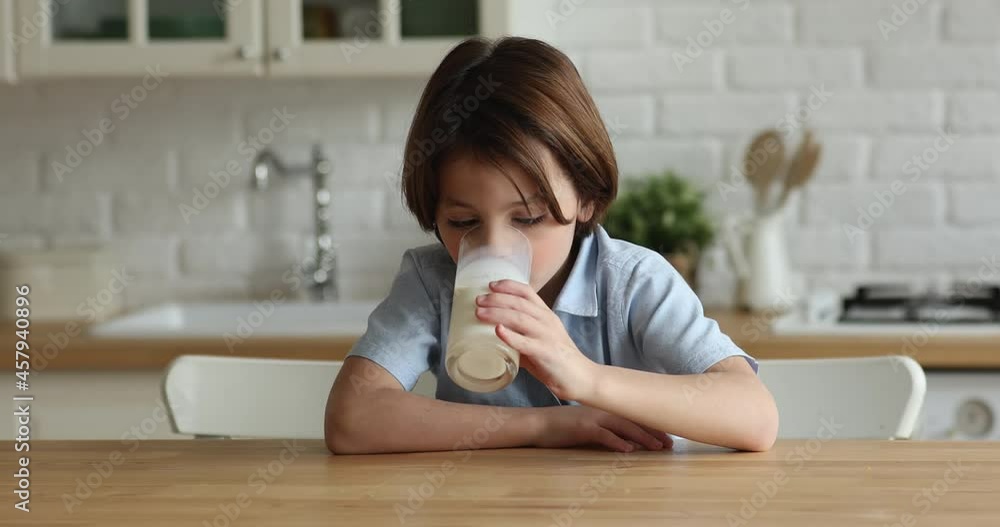 Adorable thirsty hungry little 7s child boy drinking glass of fresh organic milk or tasting delicious yoghurt, sitting at table in modern kitchen, healthy lifestyle, nutritional beverage concept. Adorable thirsty hungry little 7s child boy drinking glass of fresh organic milk or tasting delicious yoghurt, sitting at table in modern kitchen, healthy lifestyle, nutritional beverage concept.