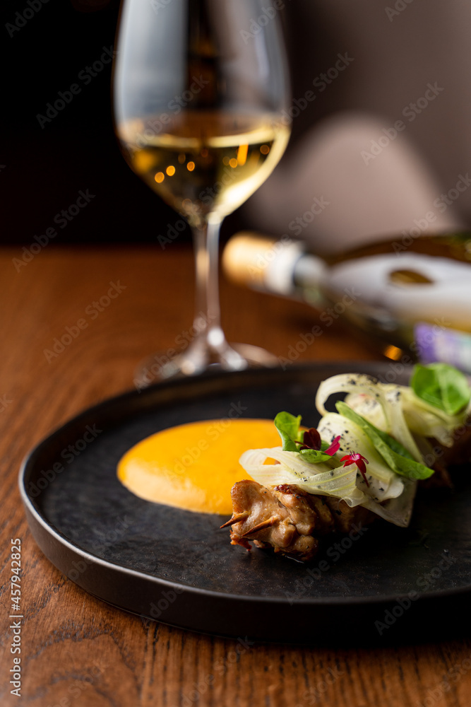 Chicken breast shish kebab with mango sauce on a black plate with a glass of white wine Chicken breast shish kebab with mango sauce on a black plate with a glass of white wine