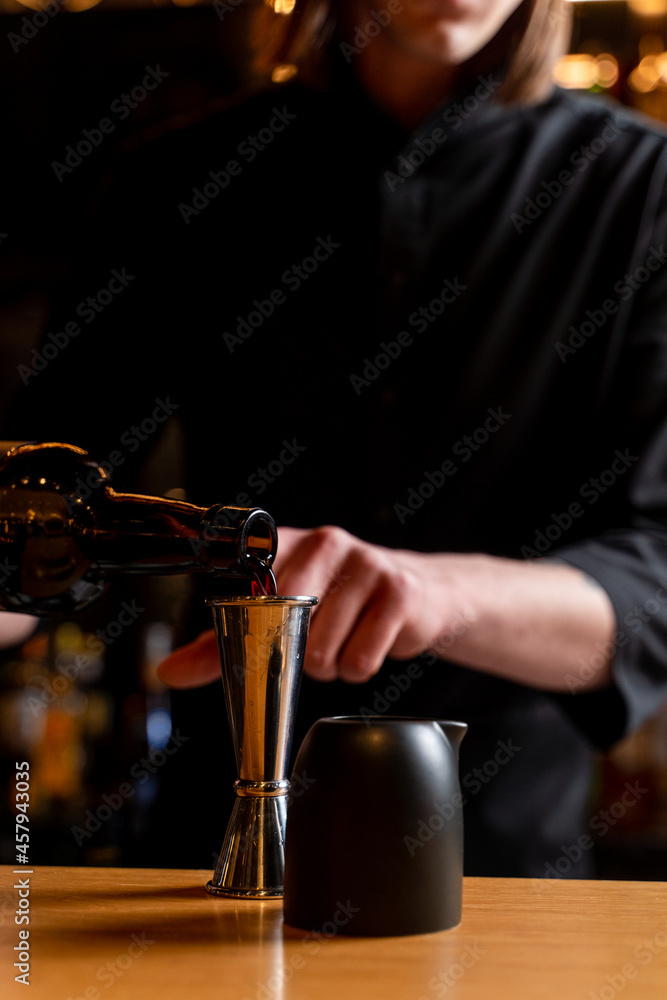 Bartender is making a cocktail, hands only visible, wooden bar counter