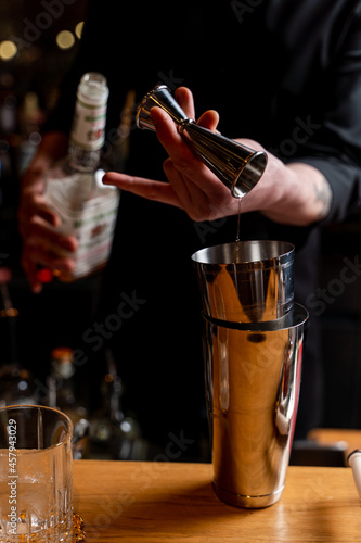 Bartender is making a cocktail in a dark bar of a restaurant  male hands only visible