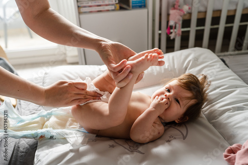 Fototapet Small caucasian baby girl or boy lying on the bed in bright room while hands of