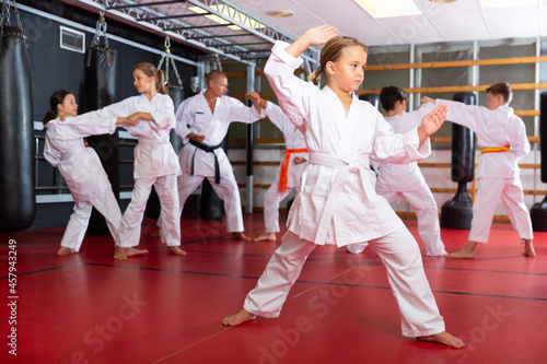 Female karate fighter in white kimono, combat stance. Children in a pair practice karate