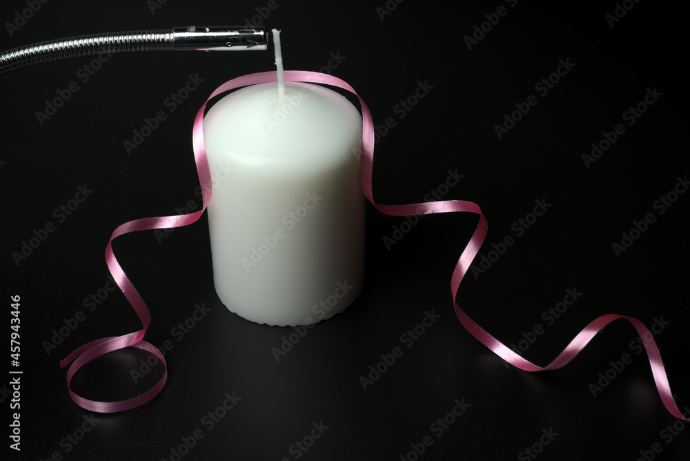 Obraz premium I light a large white candle with a pink ribbon on a black background.