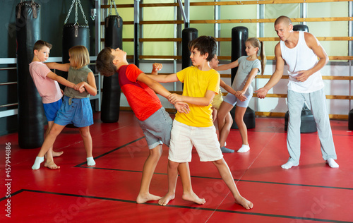 Preteen children practicing in pair self-defence movements with male trainer supervision