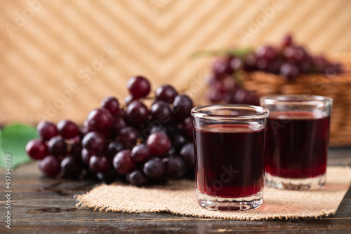Fotografia Red grape juice in a glass with fresh grape on wooden background, Healthy drink,