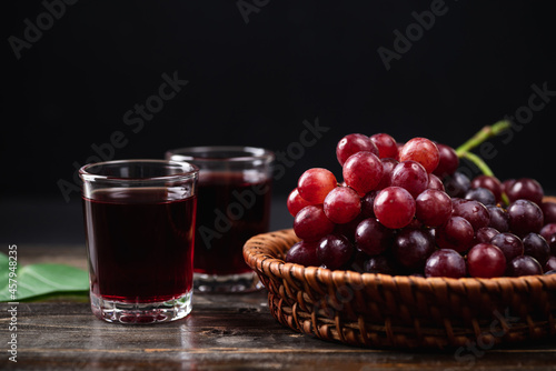 Fotografía Red grape juice in a glass with fresh grape in a basket on wooden background, He